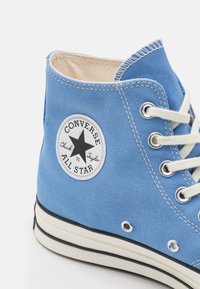 Sneaker alta in tela blu con lacci bianchi, suola in gomma nera e un marchio circolare che mostra il logo "Converse All Star".