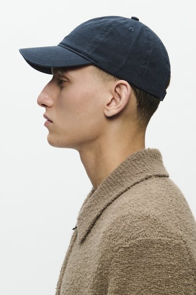 Căciulă de baseball bleumarin cu visieră curbată, fabricată din bumbac. Purtați-o cu o jachetă texturată bej, cu guler și o croială lejeră.
