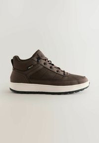 Braune Mid-Top-Sneaker mit weißer Sohle, schwarzer Profilsohle, Schnürung vorne und Cordura-Stoffetikett an der Seite.