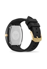 Reloj con correa de silicona negra y caja rectangular de acero inoxidable plateado, con herrajes dorados y funda grabada. Cuenta con un cierre de hebilla sencillo.