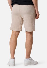 Shorts texturés beiges avec une taille élastique, dotés d'une poche arrière et associés à des sneakers blanches. Détails avec un motif subtil.