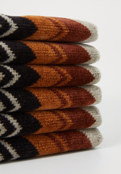 O grămadă de prosoape cu modele ce prezintă designuri în zigzag în nuanțe de portocaliu, maro și negru, cu o textură moale și capete gri; decorative și funcționale.