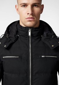 Czarna ocieplana kurtka z zapięciem na zamek, regulowanym kapturem, dwiema kieszeniami na zamek na klatce piersiowej oraz teksturowanym wykończeniem materiału. Srebrne akcenty metalowe.