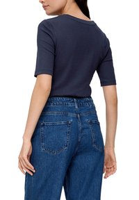 Granatowa, prążkowana koszulka z krótkim rękawem, dopasowany krój, połączona z niebieskimi dżinsami z wysokim stanem, posiadającymi tylne kieszenie i wyblakłą teksturę.
