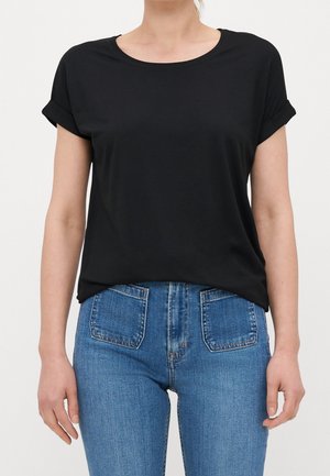 Personne portant un t-shirt noir uni à manches courtes, rentré dans un jean bleu taille haute avec des poches plaquées à l'avant.