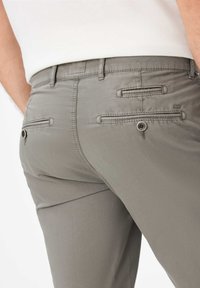 Pantaloni grigi con una texture liscia, dotati di due tasche posteriori con chiusura a bottone e dettagli cuciti. Logo del marchio discreto visibile.
