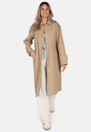 Beige trench coat with a collared neckline, buttons, side pockets, and loose fit. Worn over a striped top and cream trousers. Smooth texture.