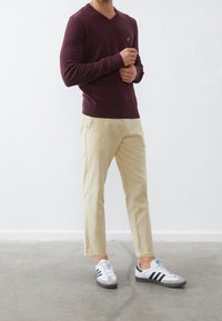 Suéter v-neck burdeos, pantalones beige ajustados y zapatillas blancas con rayas negras y acentos grises. Textura suave, diseño casual.