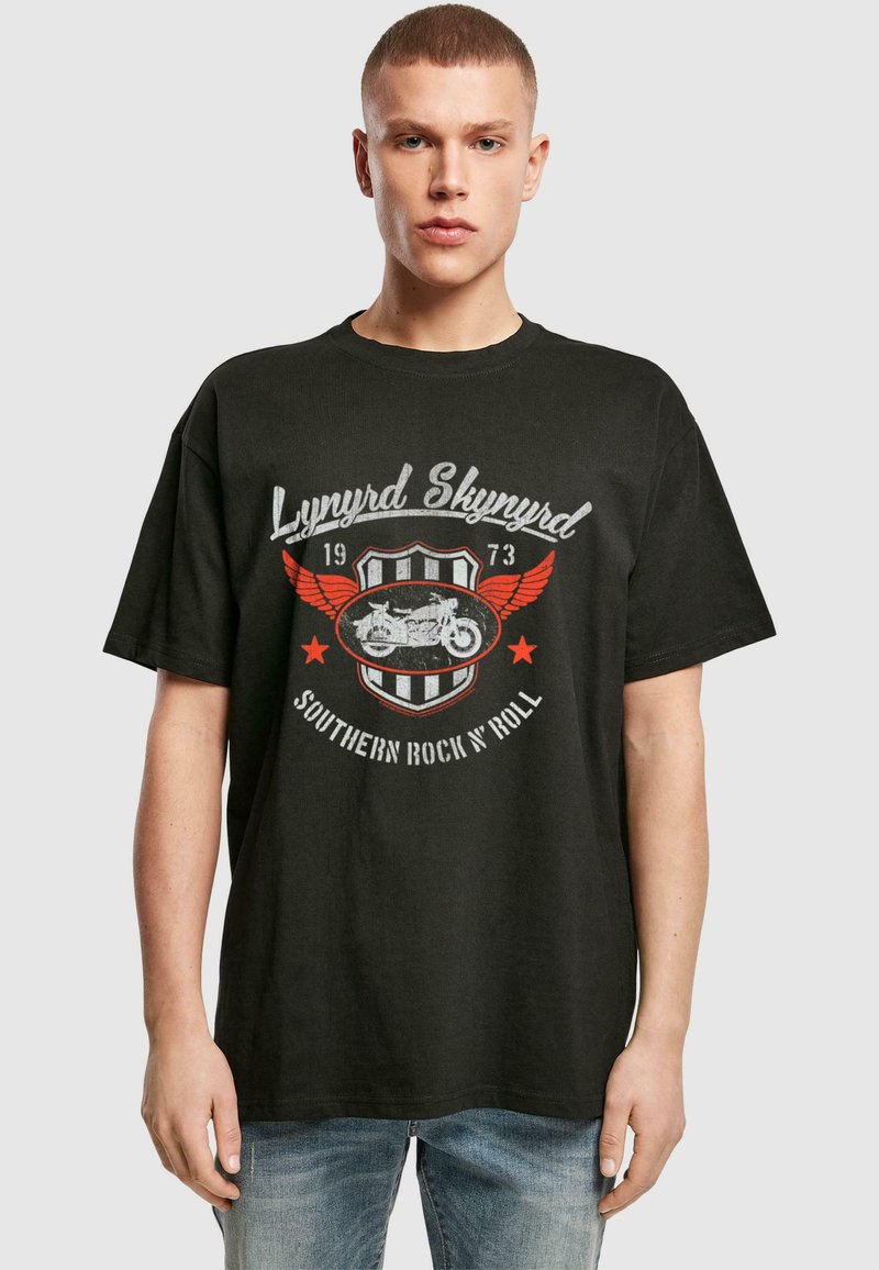 Must t-särk mustast puuvillast, millel on Lynyrd Skynyrdi graafika punaste ja valgete detailidega, kilbi kujunduses, koos kulunud mootorratta illustratsiooniga.