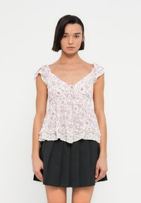 Μπλούζα με floral σχέδιο σε ανοιχτό ροζ χρώμα, με βολάν στα κοντά μανίκια και ντεκολτέ σε σχήμα V, με στρωμένο τελείωμα, συνδυασμένη με φούστα πλισέ σε μαύρο χρώμα.