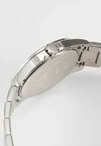 Orologio in acciaio inossidabile argento con cassa rotonda, lunetta strutturata, corona e bracciale a maglie. Superficie liscia e dettagli incisi sul retro.