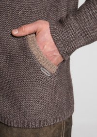 Gestrickter Pullover in dunkelbraun mit einem strukturierten Muster, ergänzt durch einen hellbraunen Taschenbesatz und einem Markenlabel auf der Tasche.