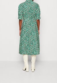 Zielona sukienka w kwiaty z krótkimi rękawami, z talią podkreśloną w pasie, długości do kolan, uszyta z lekkiego materiału. Noszona z białymi, do kolan sięgającymi botkami.