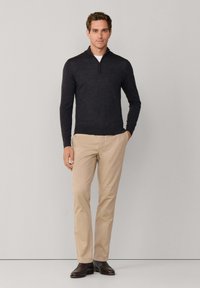 Donkergrijze gebreide pullover met lange mouwen en een kwart rits, gecombineerd met beige chinos en donkerbruine schoenen, gepresenteerd met een neutrale achtergrond.