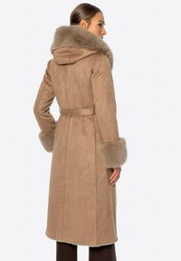 Kurtka z surowego zamszu w kolorze tan, z luksusowym kapturem wyłożonym futrem, futrzastymi mankietami oraz paskiem w talii dla dopasowanego kroju, o długości do kolan.
