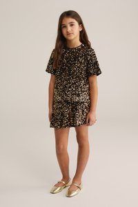 Obleka s svetlečimi elementi in kratkimi rokavi, okrašena z zlatimi in črnimi svetlečimi kamni. Ujemajoče sijajne zlate Mary Jane čevlje. Preprost dizajn krila.