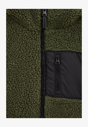 Zelená fleecová bunda s texturovaným vnějším materiálem, černou zipovou kapsou a hladkou podšívkou, s předním zipovým uzávěrem.