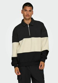 Schwarzer und cremefarbener Pullover mit hohen Kragen, Reißverschluss und großen horizontalen Farbblöcken. Gerippte Bündchen und Saum. Weicher Stoff.