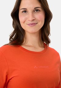 Oranges Baumwoll-T-Shirt mit rundem Halsausschnitt und langen Ärmeln. Verfügt über ein dezentes VAUDE-Logo in passender Farbe auf der Brust. Glatte Textur.