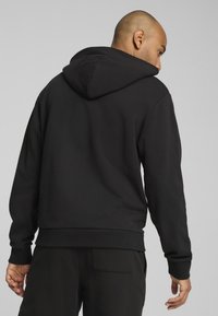 Felpa nera con cappuccio vista da dietro, caratterizzata da una trama di tessuto solido, polsini a costine e un cappuccio con lacci.