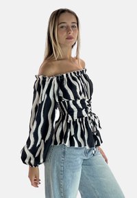 Schulterfreie Bluse in Schwarz-Weiß mit Puffärmeln, tailliert und mit Bindeband vorne, kombiniert mit Jeans.