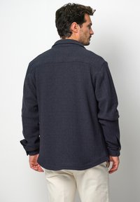 Marineblaue, strukturierte Jacke aus einem gemusterten Stoff, mit langen Ärmeln und geknöpften Manschetten. Verfügt über einen klassischen Kragen und eine lockere Passform.