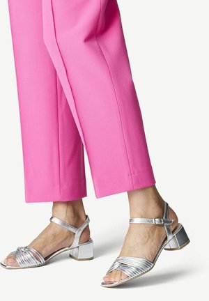 Hopeasaappaat, joissa on kierretty remmimuotoilu ja nilkkakupunki, yhdistettynä vaaleanpunaisiin, lyhennettyihin housuihin. Silkkinen metalliviimeistely.