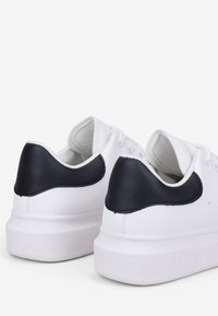 Sneaker bianchi con finitura liscia e un accento navy testurizzato sul tallone, dotati di lacci piatti e una suola leggermente rialzata.