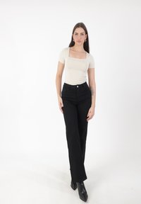 Top ajustado de manga corta beige con escote cuadrado, combinado con jeans de pierna ancha negros de cintura alta y botas negras de tacón puntiagudas.