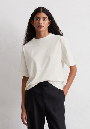 Off-white cotton t-shirt with short sleeves, a round neckline, and a relaxed fit, paired with high-waisted black trousers.