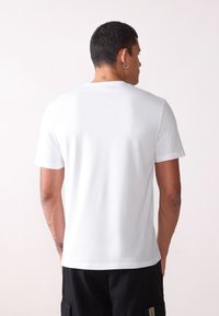 Camiseta blanca de algodón con cuello redondo y mangas cortas, que presenta una textura suave y un corte recto en el dobladillo.