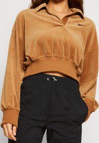 Brauner, kurzer Sweatshirt mit einer strukturierten, gerippten Verarbeitung, einem Kragen und langen Ärmeln, kombiniert mit schwarzen, elastischen Cargo-Hosen mit Gummibund.