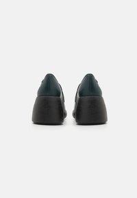 Zelené kožené wedge boty s černým dřevěným podpatkem, s elegantním tvarem a hladkým povrchem, zobrazené z zadního pohledu.