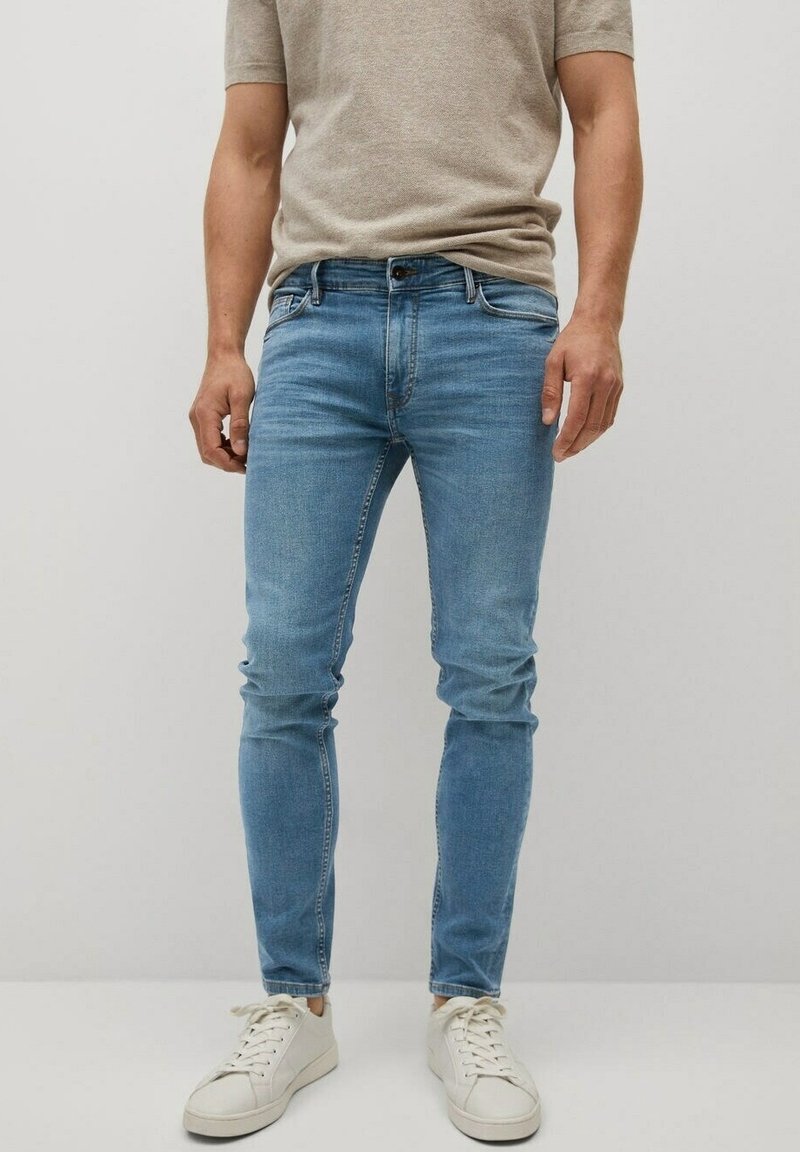 Jeans de mezclilla azul claro con un diseño ajustado, que presentan un estilo clásico de cinco bolsillos y un desgastado mínimo, combinados con zapatillas blancas.