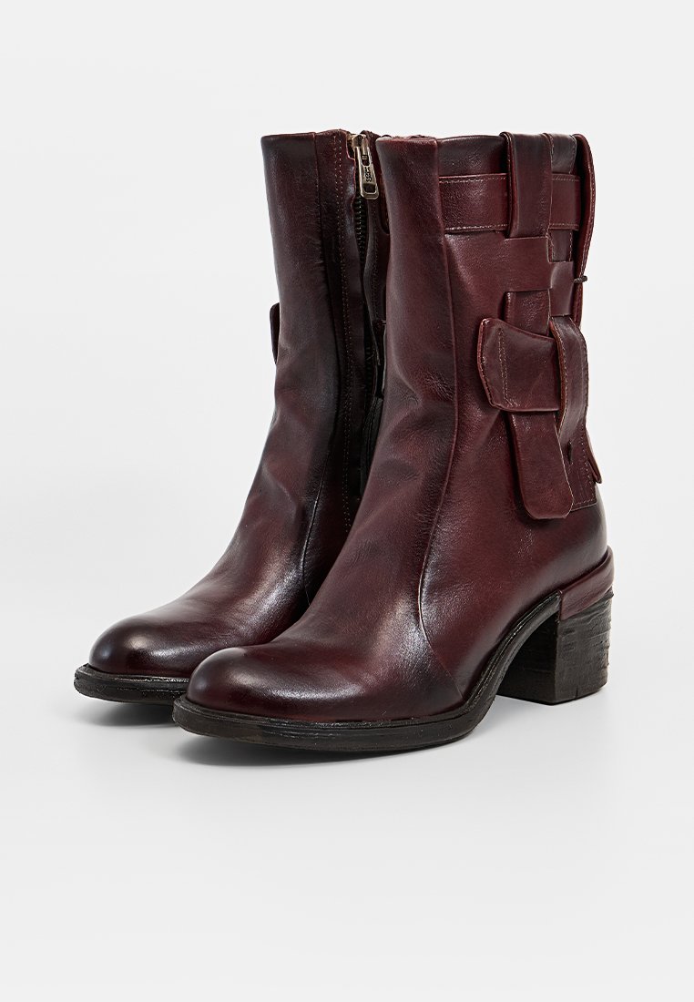 Stivaletti alla caviglia in pelle bordeaux con chiusura a zip, punta curva, tacco spesso e dettagli decorativi laterali. Texture liscia con finitura lucida.