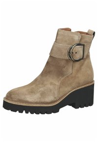 Stivale alla caviglia in suede beige con una ampia fascia e una fibbia in metallo. Suola piatta nera spessa con un battistrada testurizzato per una buona presa.