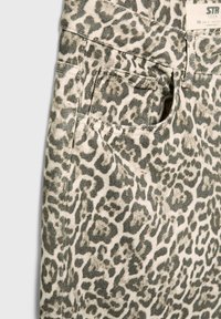 Tela vaquera con estampado de leopardo en tonos beige y gris, con un bolsillo visible y detalles de costura, diseñada en un estilo ajustado. Etiqueta de talla visible.