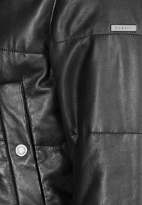 Giacca in pelle nera con texture liscia, dettagli trapuntati, chiusura con bottone argento e un sottile accento con il logo "bugatti".
