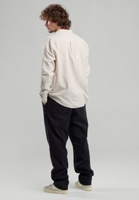 Camicia crema a strisce leggere con una vestibilità rilassata, abbinata a pantaloni neri larghi. Tessuto testurizzato e design del colletto semplice, vista da dietro.