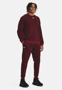 Sudadera atlética burdeos y pantalones a juego, ambos hechos de una tela texturizada, con puños acanalados y un logo de Under Armour en el pecho.