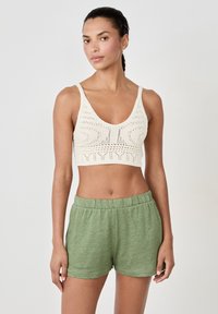 Bralette de punto en crema con un diseño estampado; combinado con pantalones cortos verdes, suaves y con cintura elástica. Textura de tela suave, ajuste casual.
