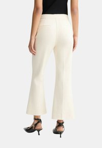 Pantaloni ampi color crema realizzati in un tessuto liscio, con tasche posteriori e fronte piatto, abbinati a scarpe con tacco nere.