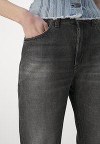 Jeans in denim nero con una finitura scolorita, caratterizzati da un design a cinque tasche e orlo sfrangiato in vita. Dettagli di cucitura sottili visibili.