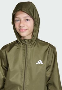 Olivovo zelená bunda so zipsom vpredu, kapucňou na šnúrku a bielymi logovými akcentmi. Hladký, ľahký materiál s priliehavým strihom.