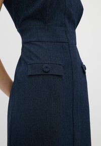 Dunkelblaues Denimkleid mit tailliertem Schnitt, seitlichen Knöpfen und glatter Textur. Die Farbe ist tiefblau mit dezenten Steppnähten.