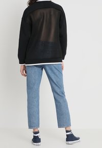 Sudadera negra con espalda de malla, mangas largas y puños acanalados, combinada con vaqueros rectos azul claro y zapatillas náuticas.