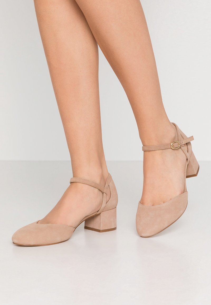 Chaussures à talons blocs en suède beige avec un design à bout pointu, dotées d'une fine bride à la cheville et d'une finition texturée.