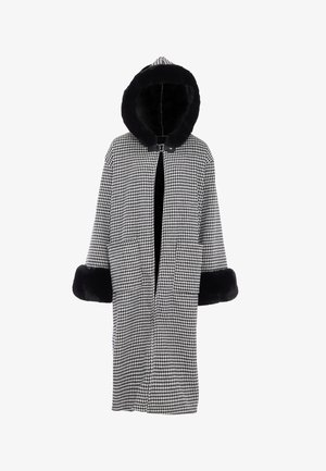 Kabát s kostkovaným vzorem ve stylu houndstooth, s černou kapucí z kožešiny, širokými rukávy a bočními kapsami. Hlavní látka je pevně tkaná v černé a bílé barvě.