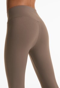 Hochtaillierte Leggings in einem gedämpften Braunton. Hergestellt aus einem glatten, dehnbaren Stoff mit flachen Nähten und einem markierten Bund.