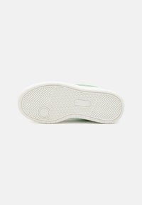 Semelle de sneaker blanche avec accent vert, surface en caoutchouc texturée, motif en chevron et détail de semelle circulaire pour l'adhérence.